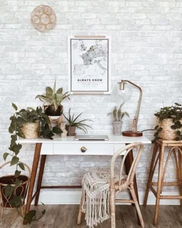 Elegantní domácí kancelář s retro dřevěným stolem, kobercem boho, nástěnnými řemesly, spoustou pokojových rostlin: kaktusy a sukulenty